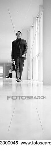 Stock Photography - Businessman walking in hallway, b&w, vertical. Fotosearch