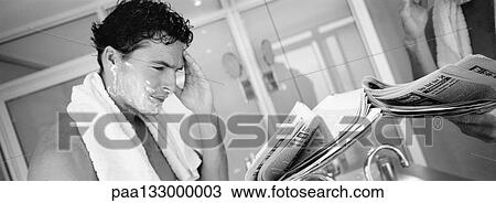 Stock Image - Man shaving and reading paper in bathroom, b&w, panoramic view. Fotosearch