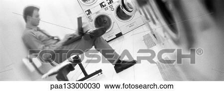 Man sitting and using laptop in laundrymat, b&w, panoramic view View Large Photo Image Stock Image - Man sitting and using laptop in laundrymat, b&w, panoramic view. Fotosearch