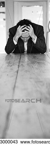 Man sitting at end of table holding head in hands, b&w, vertical View Large Photo Image Stock Image - Man sitting at end of table holding head in hands, b&w, vertical. Fotosearch