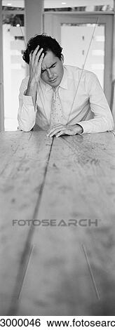 Man sitting at end of table holding head with hand, b&w, vertical View Large Photo Image Stock Photograph - Man sitting at end of table holding head with hand, b&w, vertical. Fotosearch