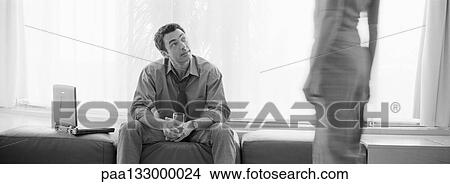 Man sitting holding glass, looking up at woman standing, mid section, b&w, panoramic view View Large Photo Image Picture - Man sitting holding glass, looking up at woman standing, mid section, b&w, panoramic view. Fotosearch