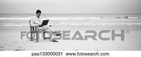 Man sitting in chair on beach using laptop, b&w, panoramic view View Large Photo Image Stock Image - Man sitting in chair on beach using laptop, b&w, panoramic view. Fotosearch