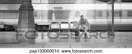 Man sitting in seat on train platform, using laptop, b&w, panoramic view View Large Photo Image Picture - Man sitting in seat on train platform, using laptop, b&w, panoramic view. Fotosearch