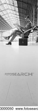 Man sitting in train station, reading newspaper, b&w, vertical View Large Photo Image Stock Image - Man sitting in train station, reading newspaper, b&w, vertical. Fotosearch