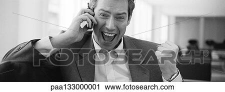 Stock Image - Man talking on cell phone, making fist and yelling with joy, b&w, panoramic view. Fotosearch