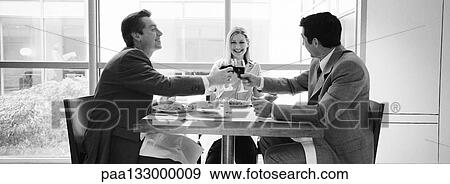 Two businessmen and woman sitting at table clinking glasses, b&w, panoramic view View Large Photo Image Stock Photo - Two businessmen and woman sitting at table clinking glasses, b&w, panoramic view. Fotosearch