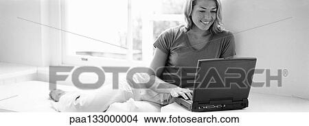 Woman lounging by window, using laptop, b&w, panoramic view View Large Photo Image Picture - Woman lounging by window, using laptop, b&w, panoramic view. Fotosearch