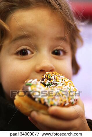 Stock Photo - Child eating doughnut with sprinkles, close-up. Fotosearch