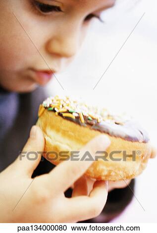 Stock Image - Child holding doughnut, close-up.. Fotosearch
