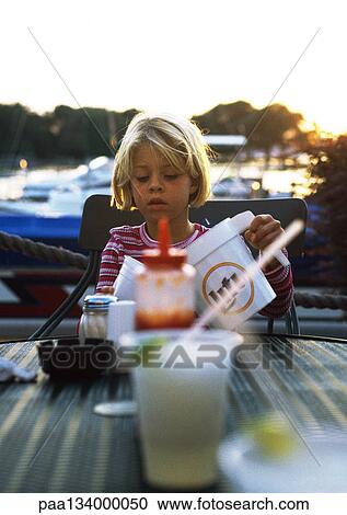 Stock Image - Child sitting at table, pouring drink.. Fotosearch