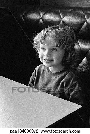 Stock Image - Child sitting at table smiling, portrait, b&w.. Fotosearch