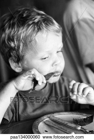 Stock Image - Little boy eating at table, portrait, b&w.. Fotosearch