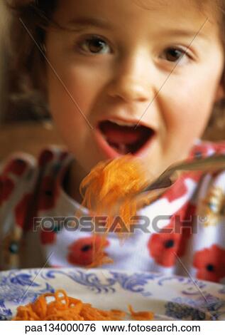 Stock Photograph - Little girl eating shredded carrots, portrait.. Fotosearch