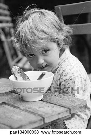 Little girl sitting at table with bowl, looking into camera, b&w. View Large Photo Image Stock Photo - Little girl sitting at table with bowl, looking into camera, b&w.. Fotosearch