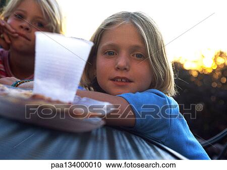 Stock Image - Two girls sitting at table, plastic cup in foreground.. Fotosearch
