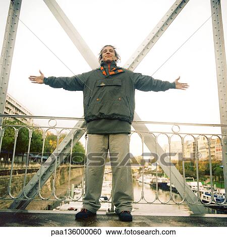 Man standing on bridge wearing winter clothes with arms stretched out View Large Photo Image Stock Image - Man standing on bridge wearing winter clothes with arms stretched out. Fotosearch