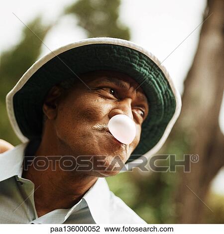 Stock Image - Portrait of man blowing a bubble with chewing gum. Fotosearch