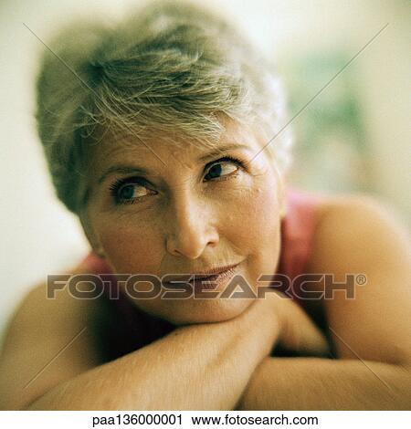 Stock Image - Portrait of mature woman arms crossed under chin, close-up. Fotosearch