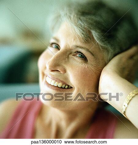 Stock Image - Portrait of mature woman smiling with head resting in hand . Fotosearch