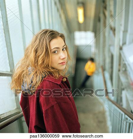 Stock Photo - Woman looking over shoulder while standing at top of staircase, portrait. Fotosearch