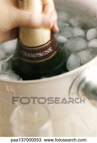 Stock Image - Hand holding bottle of Champagne in bucket.. Fotosearch