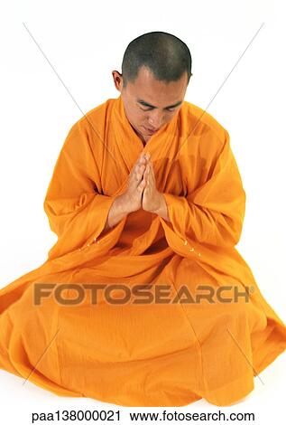 Stock Image - Buddhist monk sitting, meditating with hands together, high angle view. Fotosearch