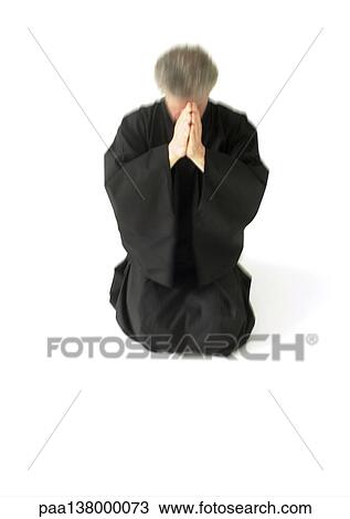 Stock Image - Man kneeling on floor, hands together in front of face. Fotosearch