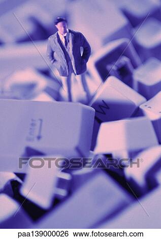 Stock Photograph - Small toy figure standing in pile of keyboard keys, close-up. Fotosearch