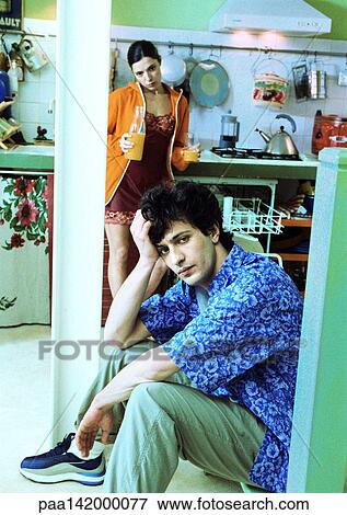 Couple in kitchen, man sitting with head on hand, looking into camera, woman standing and holding juice. View Large Photo Image Stock Photo - Couple in kitchen, man sitting with head on hand, looking into camera, woman standing and holding juice.. Fotosearch