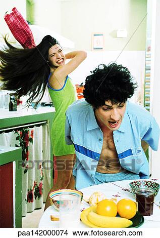 Man at breakfast table, woman swinging kitchen towel at man. View Large Photo Image Picture - Man at breakfast table, woman swinging kitchen towel at man.. Fotosearch