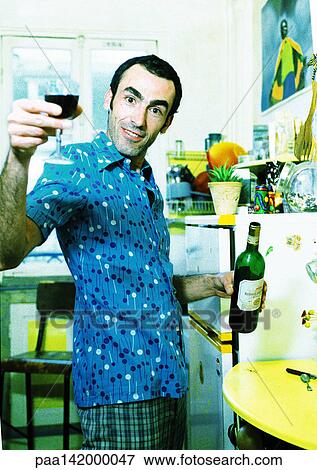 Man in kitchen holding bottle of wine, raising his glass, portrait. View Large Photo Image Stock Photo - Man in kitchen holding bottle of wine, raising his glass, portrait.. Fotosearch
