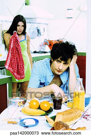 Man sitting at breakfast table, woman standing behind man, holding kitchen towel. View Large Photo Image Stock Image - Man sitting at breakfast table, woman standing behind man, holding kitchen towel.. Fotosearch