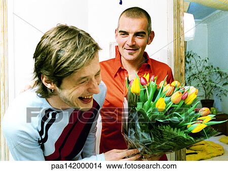 Picture - Two men smiling and laughing, one holding bouquet of flowers, portrait.. Fotosearch