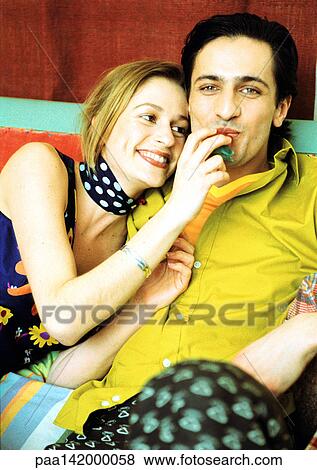 Stock Photo - Young couple sitting together, woman's hand at man's mouth, portrait.. Fotosearch