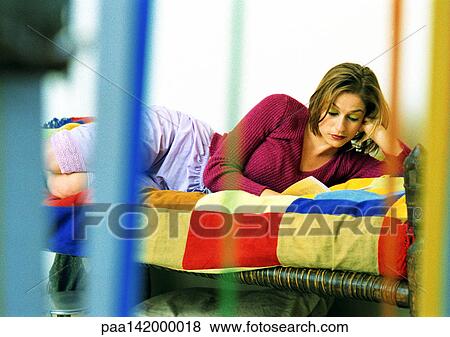 Stock Photo - Young woman lying on bed reading.. Fotosearch