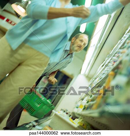Stock Image - Man and woman in supermarket, man holding shopping basket. Fotosearch