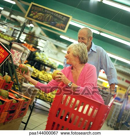 Mature couple in supermarket, woman in shopping cart choosing fruit View Large Photo Image Stock Photo - Mature couple in supermarket, woman in shopping cart choosing fruit. Fotosearch