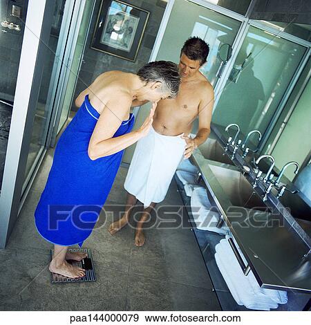 Mature couple standing in bathroom, woman weighing herself View Large Photo Image Stock Photo - Mature couple standing in bathroom, woman weighing herself. Fotosearch