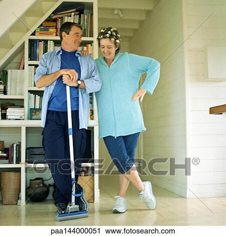Stock Image - Mature couple standing side by side, man holding broom. Fotosearch