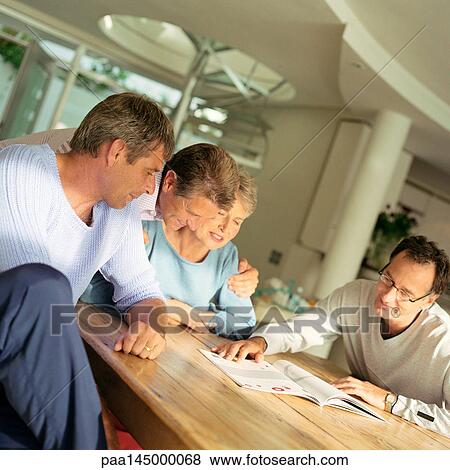 Four mature people sitting at table, looking at magazine View Large Photo Image Stock Photo - Four mature people sitting at table, looking at magazine. Fotosearch