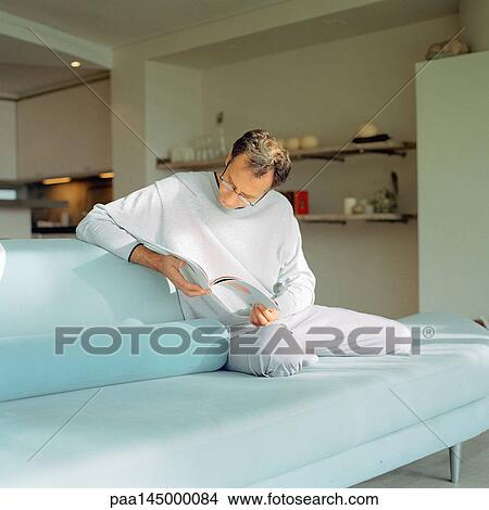 Man sitting on sofa, reading View Large Photo Image Picture - Man sitting on sofa, reading. Fotosearch