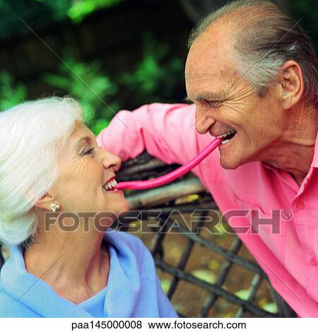 Stock Photo - Mature couple face to face, each with one end of piece of candy in mouth between them. Fotosearch