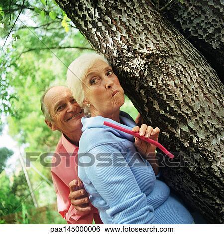 Mature man and woman standing behind tree View Large Photo Image Stock Photograph - Mature man and woman standing behind tree. Fotosearch
