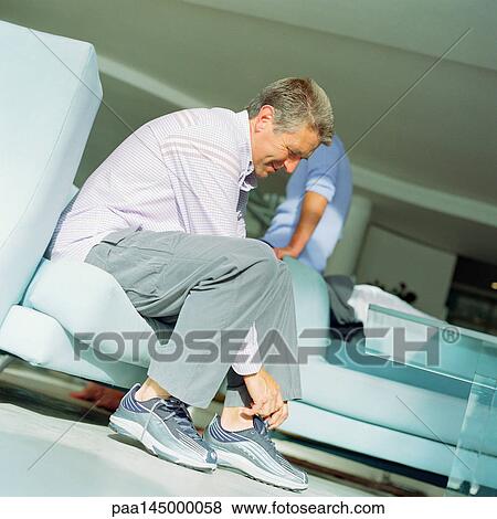 Mature man putting on shoes, second person leaning on arm of sofa, side view View Large Photo Image Stock Photo - Mature man putting on shoes, second person leaning on arm of sofa, side view. Fotosearch
