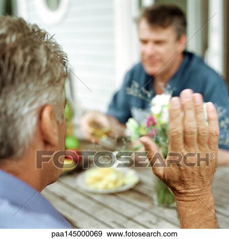 Mature man raising hand, sitting across from second man at table View Large Photo Image Stock Photo - Mature man raising hand, sitting across from second man at table. Fotosearch