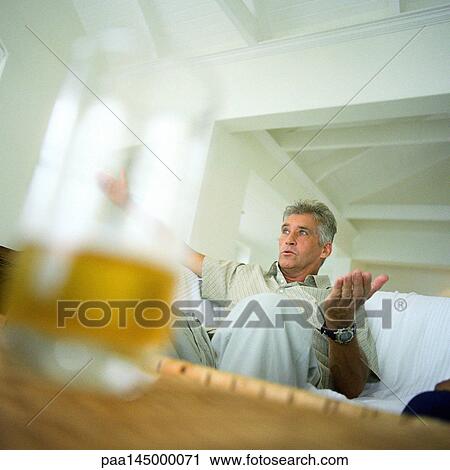 Mature man sitting on sofa, blurred drink in foreground View Large Photo Image Stock Image - Mature man sitting on sofa, blurred drink in foreground. Fotosearch