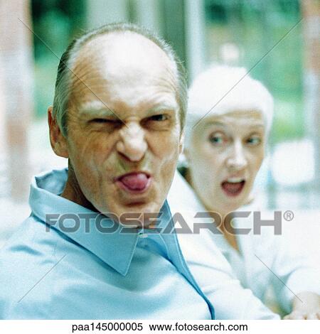 Mature man sticking out tongue, woman in background View Large Photo Image Stock Photography - Mature man sticking out tongue, woman in background. Fotosearch