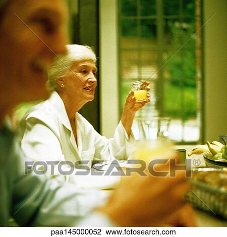 Mature woman sitting at table, holding glass, man blurred in foreground View Large Photo Image Stock Image - Mature woman sitting at table, holding glass, man blurred in foreground. Fotosearch