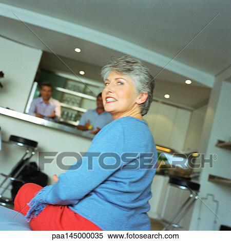 Mature woman sitting, looking over shoulder, men standing in kitchen in background View Large Photo Image Stock Photography - Mature woman sitting, looking over shoulder, men standing in kitchen in background. Fotosearch